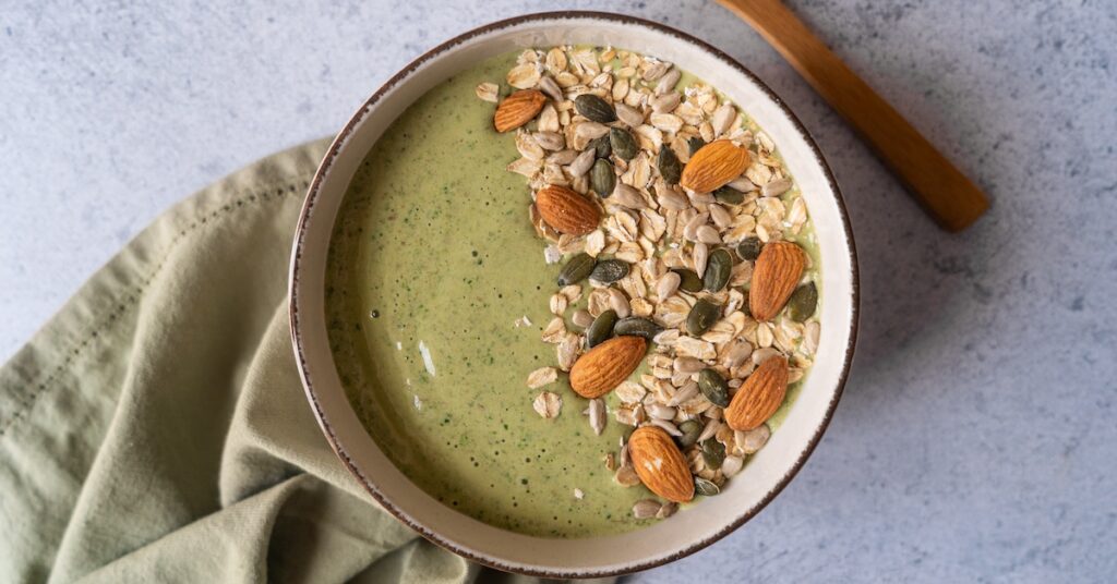 green smoothie dans un bol avec de l'avoine et des amandes