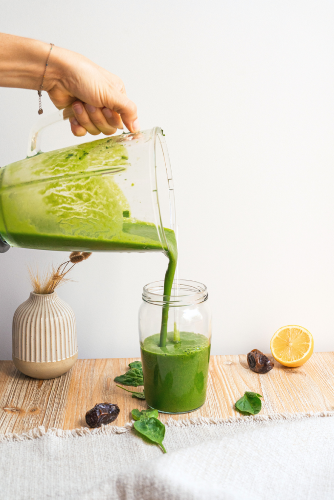 main qui verse un green smoothie du blender au verre