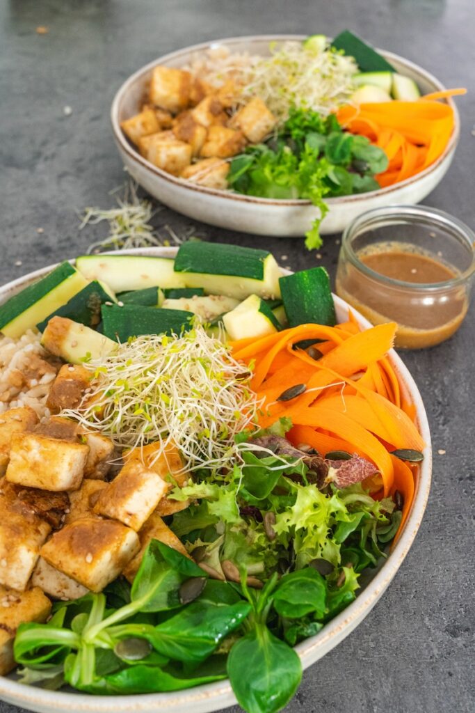 deux assiettes à base de tofu et légumes avec une sauce soja et cacahuète sur le côté